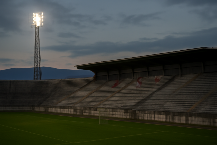 Stadion sepak bola kecil di kota Balkan saat senja dengan bendera klub di tribun